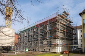 Modernisiertes Mehrfamilienhaus mit neuer Fassade und eingebauten Fenstern mit Heizglas, eingerüstet für weitere Arbeiten.